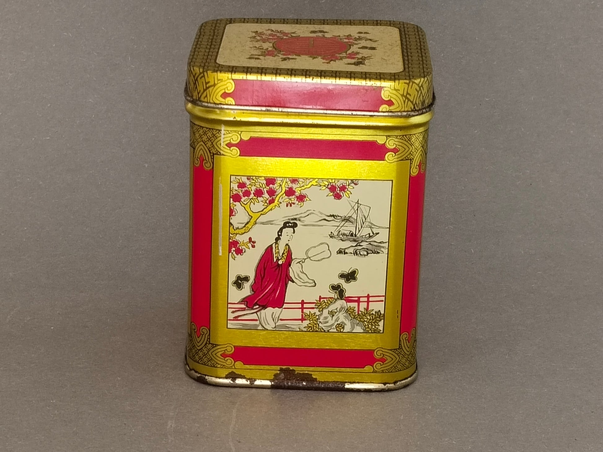 Chinoiserie-Blechdose mit Damenmotiv am See, Rostpunkte an der unteren Kante sichtbar
