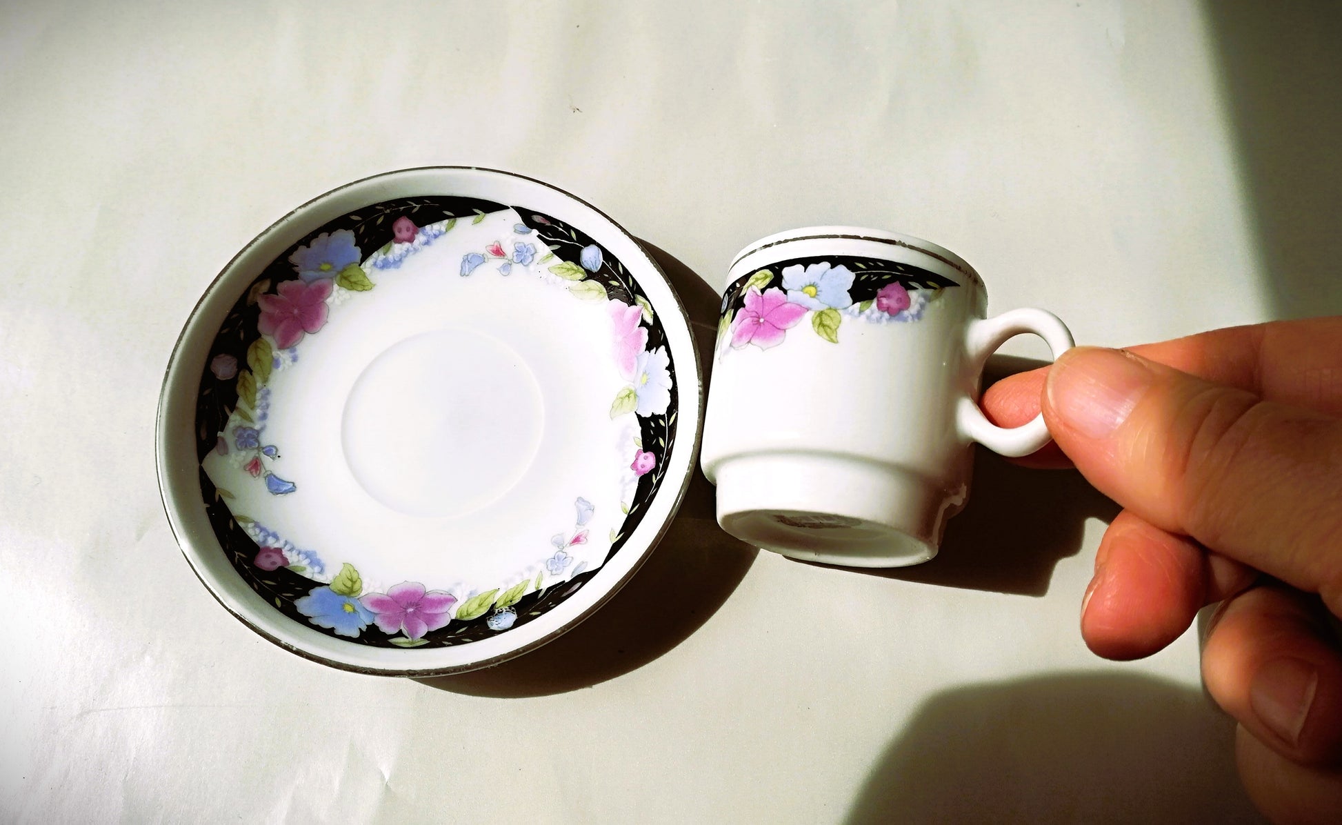 Sechsteiliges chinesisches Porzellan-Set mit bunten Blumenmotiven auf weißem Grund. Tasse liegt neben dem Teller.