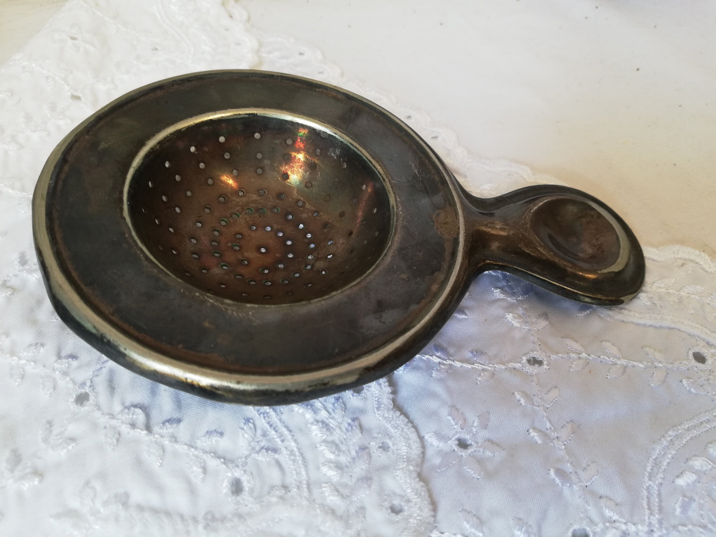Antikes Teesieb von Moritz Hacker aus versilbertem Metall mit dunkler Patina auf weißer Spitze.