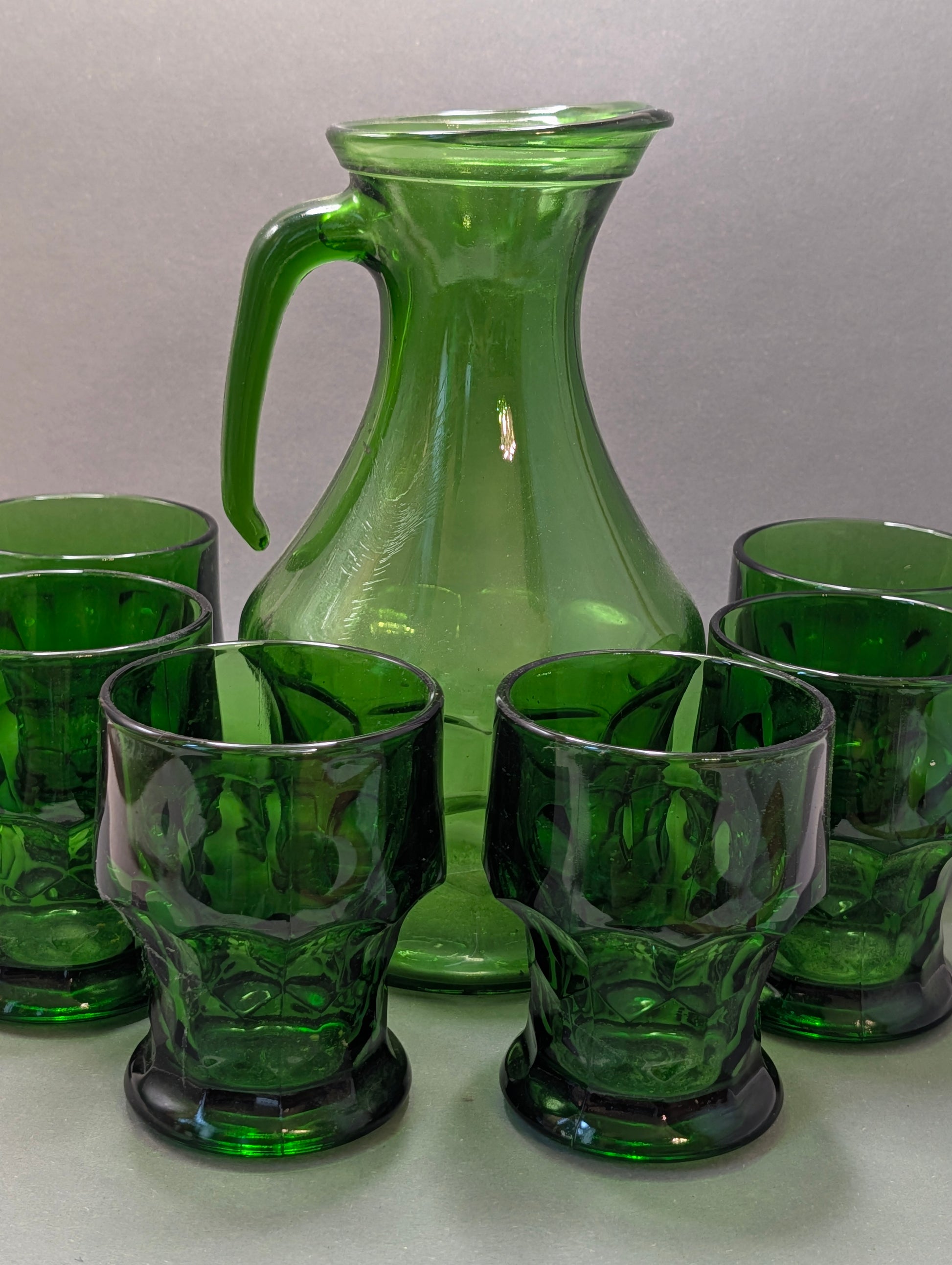 Sechs grüne Vintage-Gläser mit Honigwaben-Muster vor grüner Glaskaraffe

