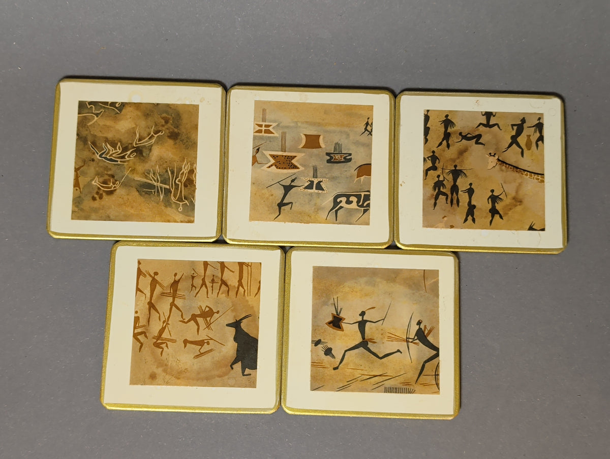 Fünf handgefertigte Vintage-Getränkeuntersetzer mit Felsmalerei-Motiven, cremeweißem Rand und Goldkante, von oben fotografiert