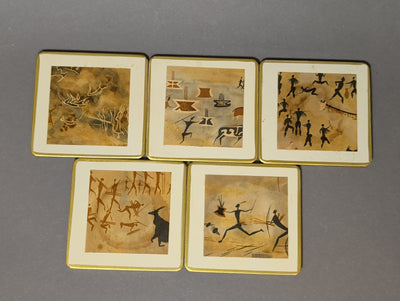Fünf handgefertigte Vintage-Getränkeuntersetzer mit Felsmalerei-Motiven, cremeweißem Rand und Goldkante, von oben fotografiert