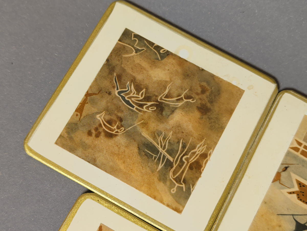 Detail Vintage-Untersetzer: helle Umrisszeichnungen gehörnter Tiere auf braun-grünem Grund, am Rand ein kleiner heller Fleck