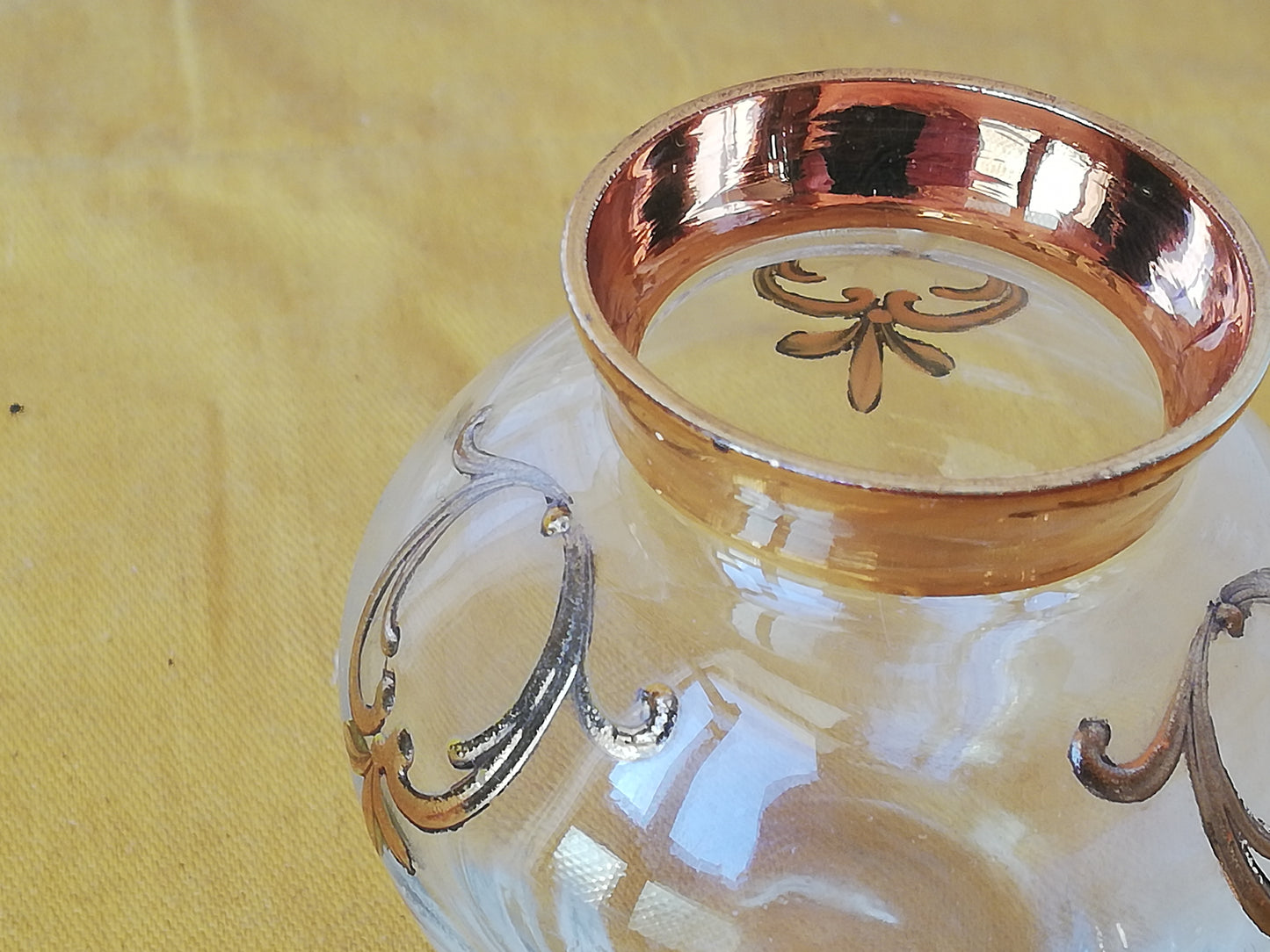 Detailaufnahme der goldenen floralen Reliefmotive auf der bauchigen Glaswand der Vase.