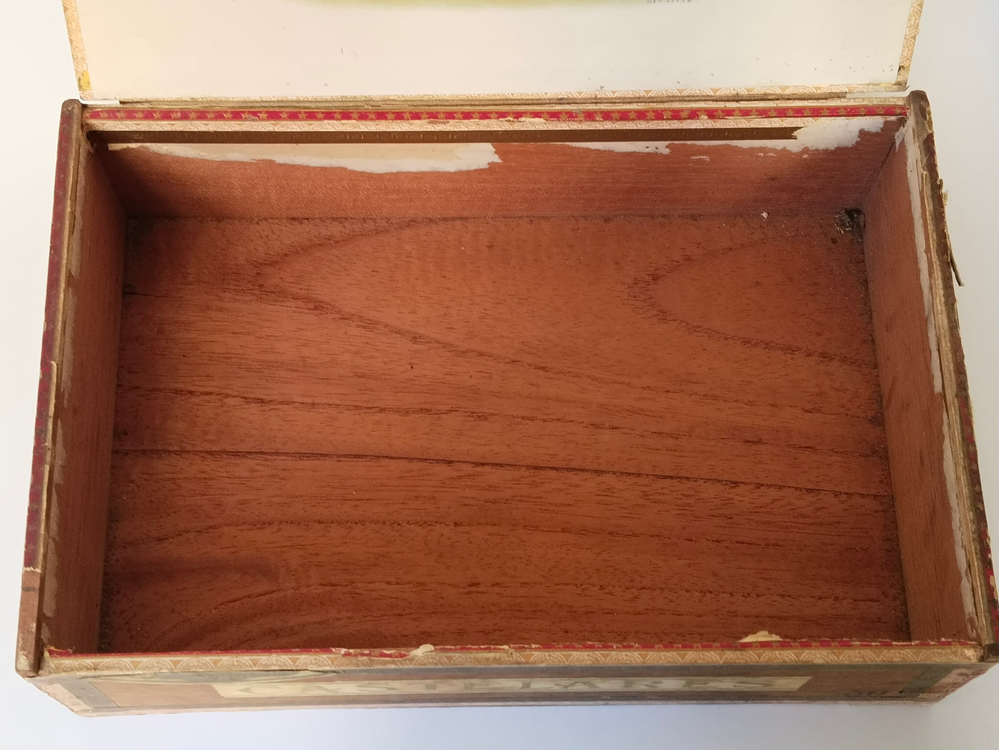 Leerer Innenraum der Zigarrenkiste mit sichtbarer Holzmaserung und teilweise fehlendem weißem Innenpapier