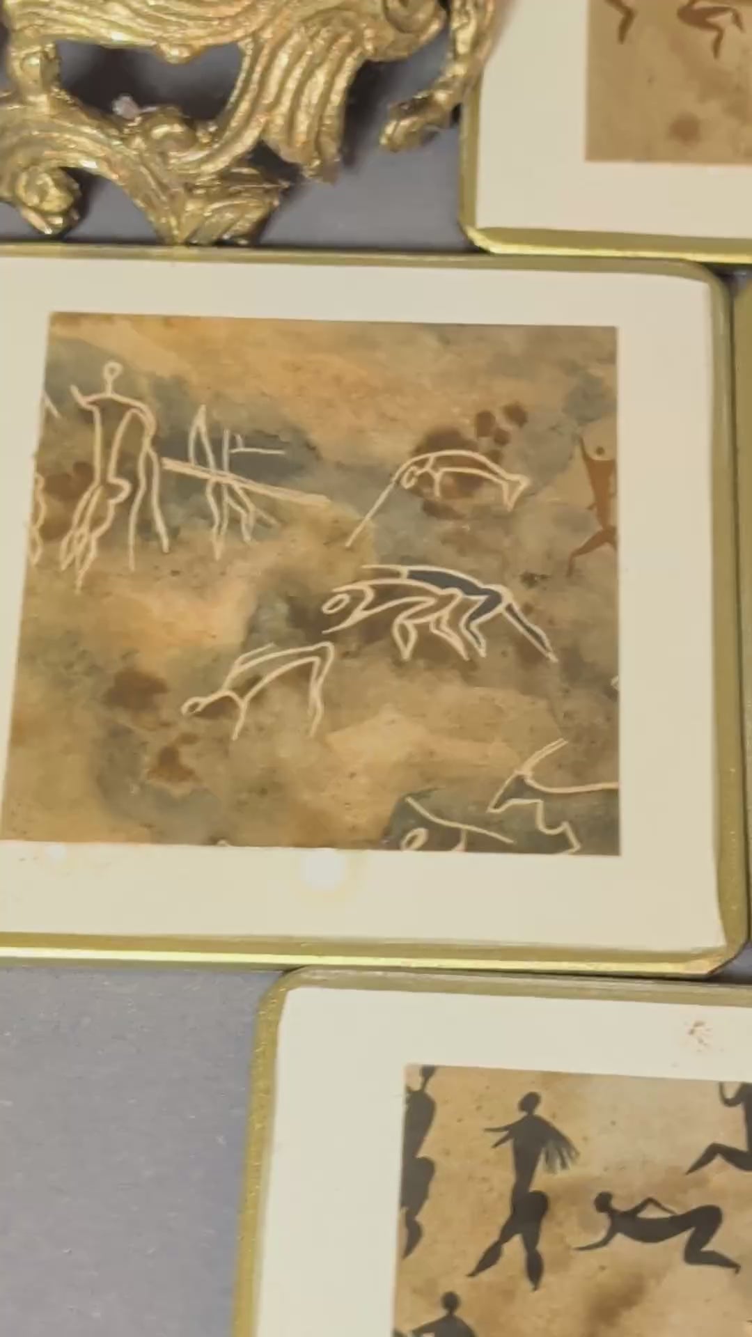 Fünf handgefertigte Vintage-Getränkeuntersetzer mit Felsmalerei-Motiven, cremeweißem Rand und Goldkante, Video.