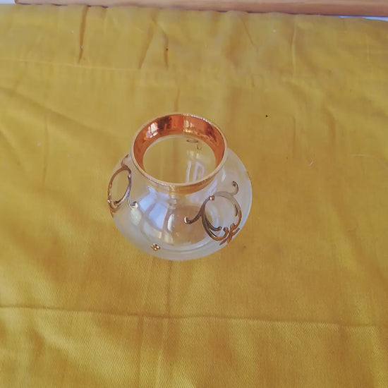 Kleine venezianische Glasvase mit goldenen Reliefs auf einem gelben Tuch vor einem gerahmten Naturbild. Video.