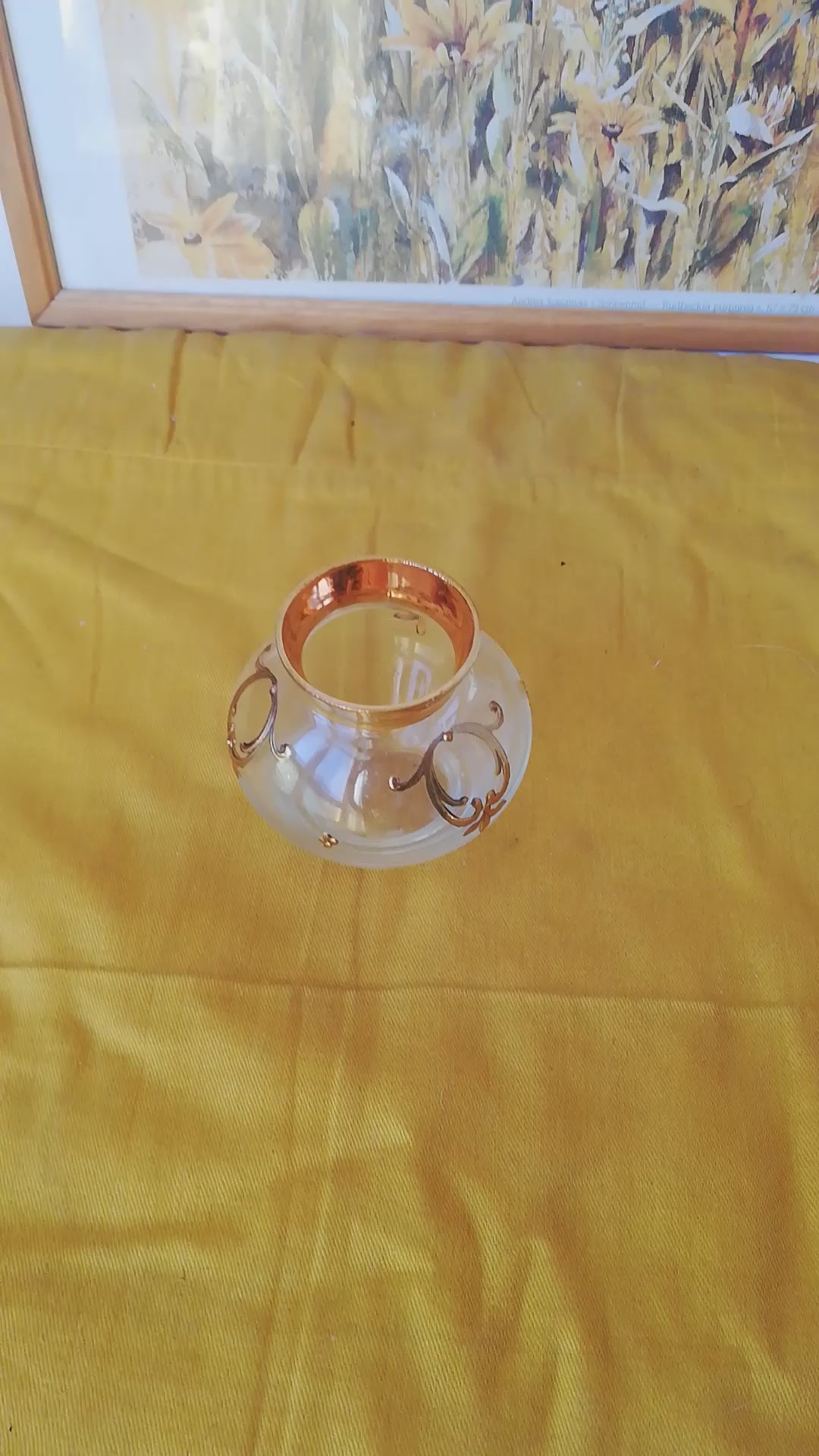 Kleine venezianische Glasvase mit goldenen Reliefs auf einem gelben Tuch vor einem gerahmten Naturbild. Video.